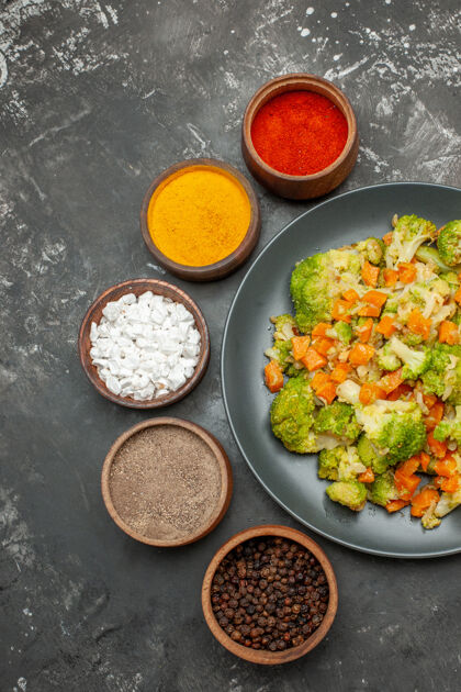 一餐健康膳食的垂直视图 黑色盘子上有花椰菜和胡萝卜 灰色桌子上有香料饮食蔬菜盘子