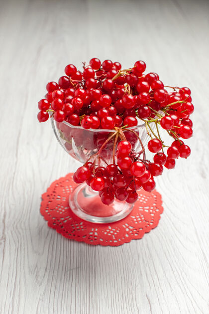 花边前视图红色葡萄干在一个水晶玻璃上的红色椭圆形蕾丝桌布上的白色木制桌子与复制空间可食用水果椭圆形桌子