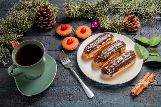 肉桂下图：白色椭圆形平板上的巧克力蛋糕 冷杉树枝和圆锥体 圣诞玩具 叉子 肉桂 一杯茶 黑木桌上的纸杯蛋糕纸杯蛋糕营养品底
