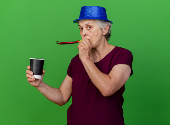 老人惊讶的戴着派对帽的老妇人拿着杯子吹着哨子惊喜杯子吹