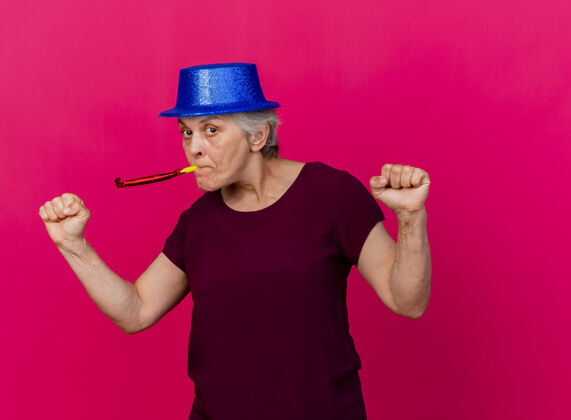 聚会自信的戴着派对帽的老太太 拳头不断地吹着粉色的口哨老人吹信心