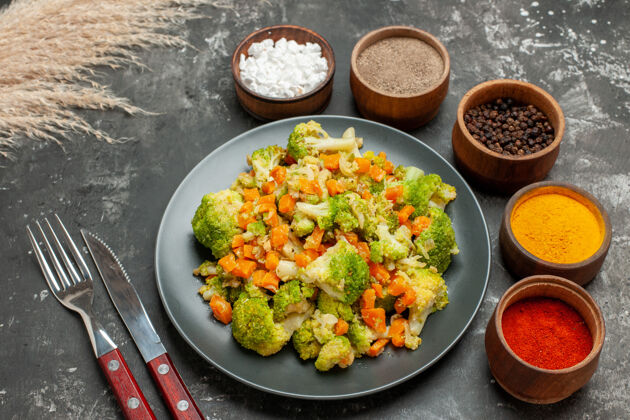 健康一餐健康餐的俯视图 在黑色盘子上放花椰菜和胡萝卜 用叉子和刀子放香料沙拉菜肴胡萝卜