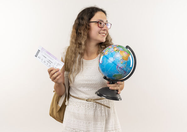 感情微笑着的年轻漂亮的女学生戴着眼镜 背着包 拿着地球仪和票 看着隔离在白墙上的一面壁板人姿势