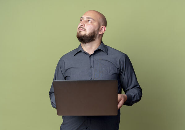 中心体贴的年轻秃头呼叫中心男子手持笔记本电脑 孤零零地看着橄榄绿的墙上姿势保持秃头