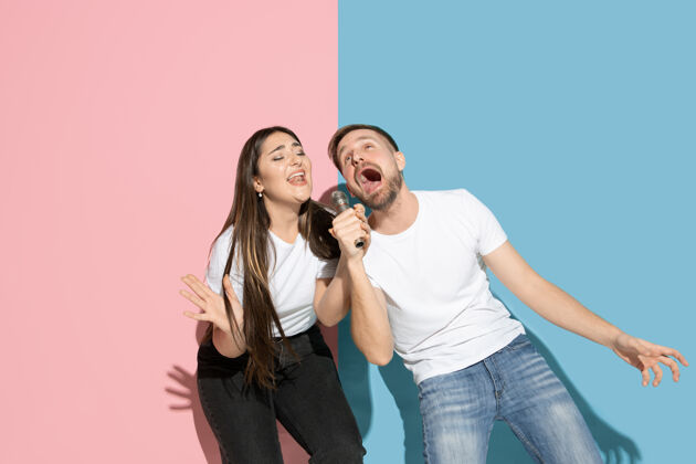 笑年轻快乐的男女穿着休闲服站在粉色 蓝色的双色墙上 唱歌在一起休闲表情