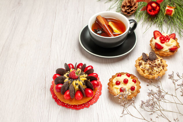 食物底部视图一杯柠檬肉桂茶浆果蛋糕馅饼和松树叶子 白色木制背景上有圣诞玩具盘子木头圣诞