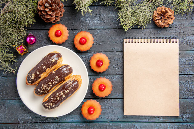 盘子俯视图白色椭圆形平板冷杉树枝上的巧克力蛋糕圣诞玩具纸杯蛋糕和黑木桌上的笔记本甜点圣诞节桌子
