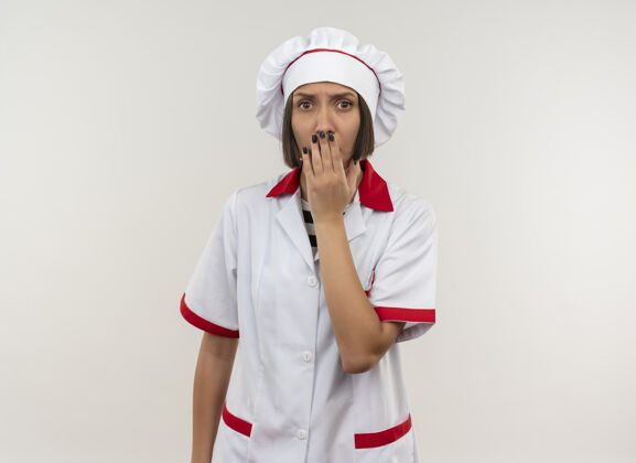 女性惊讶的年轻女厨师穿着厨师制服把手放在嘴上隔离在白墙上烹饪人人