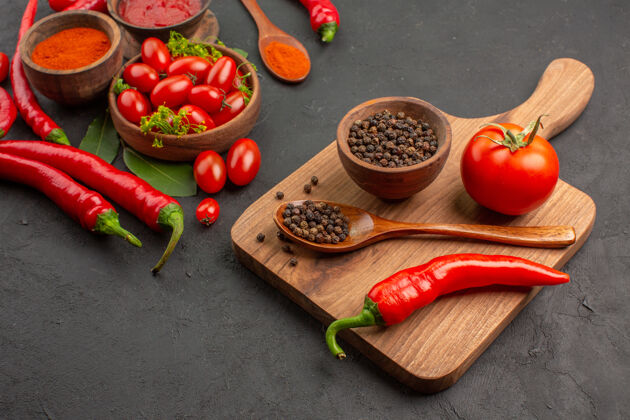 板一碗樱桃西红柿 一碗红辣椒 月桂叶 一碗黑胡椒 一个木勺 一个红胡椒 放在砧板上 背景是黑色的碗勺子食物