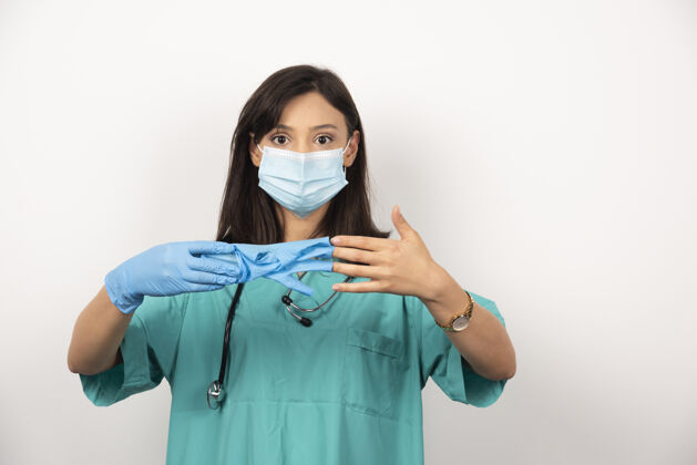 听诊器戴着医用面罩的女医生在白色背景上展示一副手套高质量照片健康保健职业