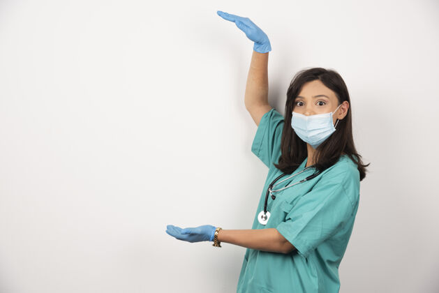 制服戴着医用面罩和手套的年轻医生手持白色背景上的空地高质量照片工作开放空间妇女