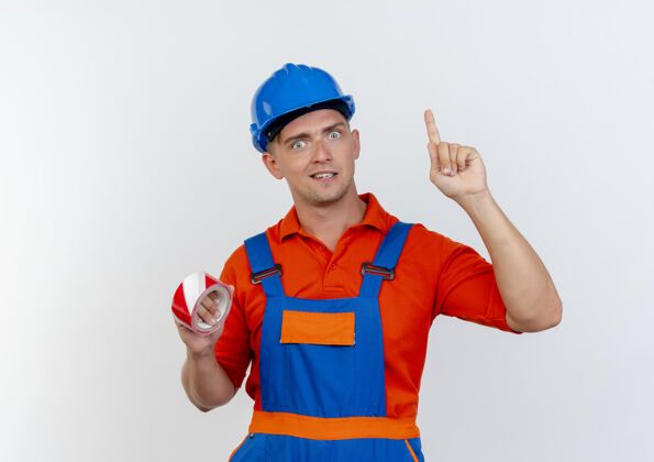 点印象深刻的年轻男性建筑工人穿着制服和安全帽举行管道胶带和点在上面背景安全头盔