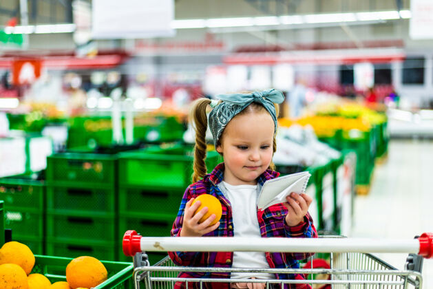 小女孩小消费者在超市购物时 正在制作购买产品清单女孩购物手推车