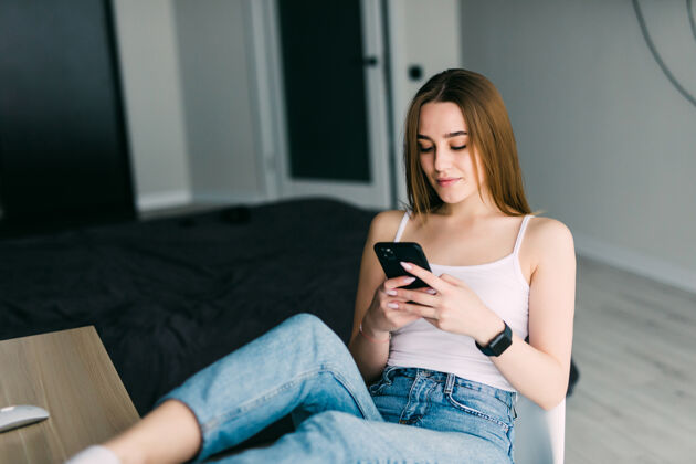 客厅坐在家里沙发上拿着手机的快乐年轻女子的画像成人互联网短信
