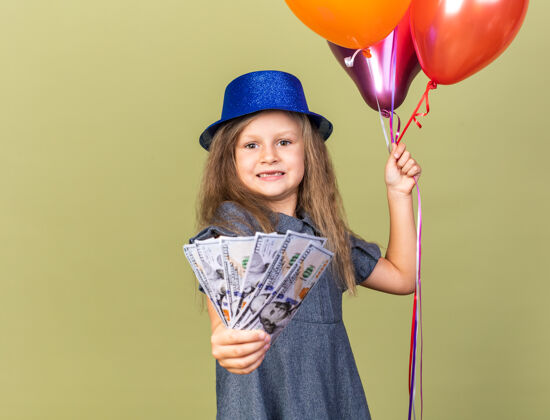 小焦急的金发小女孩 戴着蓝色派对帽 手里拿着氦气球和钱 被隔离在橄榄绿的墙上 还有复印空间生日钱举行