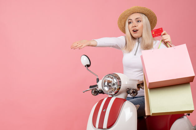 车前视图骑着轻便摩托车的年轻女士拿着卡片和购物袋抱轻便摩托车前面