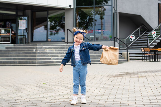可爱年轻的小女孩拿着快餐袋在咖啡馆附近的户外城市街道包