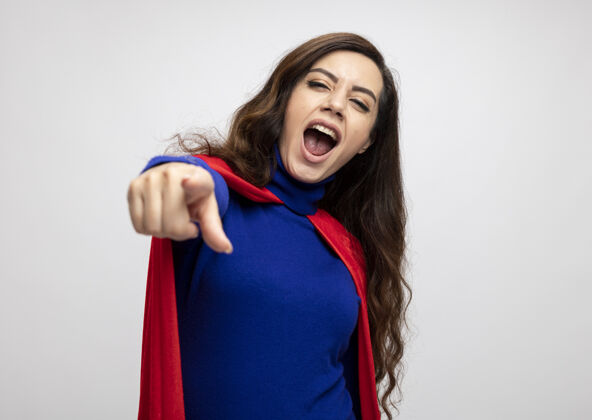 欢乐快乐的女超人用红色斗篷指着前面的白色墙壁斗篷人脸