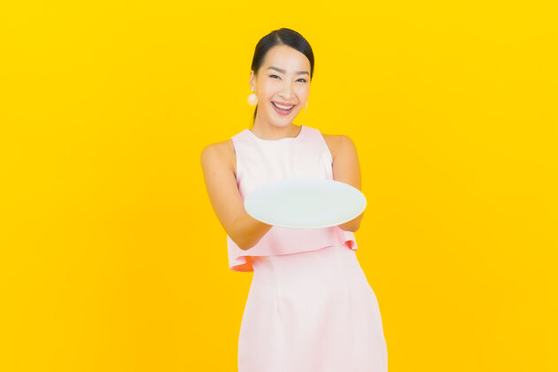 房子肖像美丽的亚洲年轻女子微笑 黄色的空盘子衣服厨师围裙