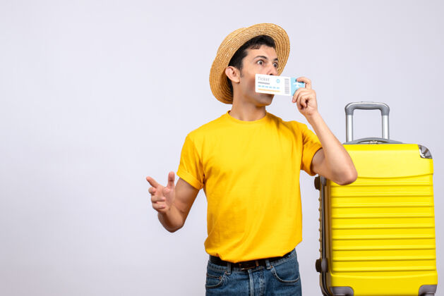 票正面图睁大眼睛的年轻游客站在拿着票的黄色手提箱旁视图持有手提箱