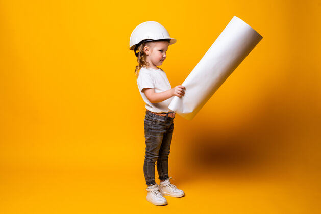 建筑师可爱的小女孩工程师 戴着头盔 把蓝弹簧隔离在黄色的墙上可爱女孩绘画