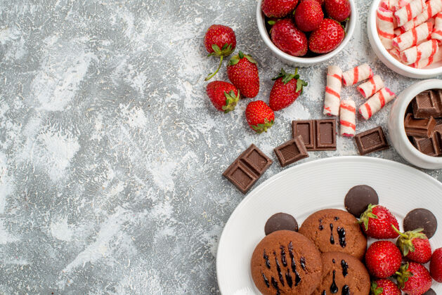 一半上半部分是白色椭圆形盘子上的曲奇草莓和圆形巧克力 灰白色桌子上的碗糖果草莓巧克力浆果新鲜碗