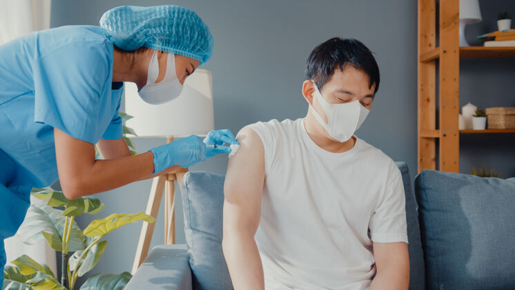 治疗年轻的亚洲女护士给男性病人注射covid-19或流感病毒疫苗戴口罩以防病毒感染访问病毒客厅