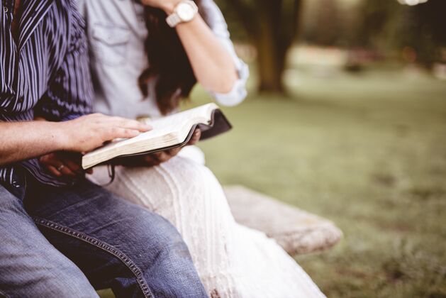 传统一对夫妇坐在公园里读圣经的特写镜头 背景模糊男人阅读年轻