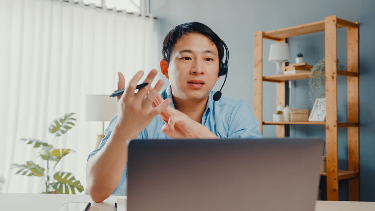 笔记本电脑年轻的亚洲商人戴着耳机用笔记本电脑和同事在客厅工作时用视频通话的方式谈论计划年轻人通话设备
