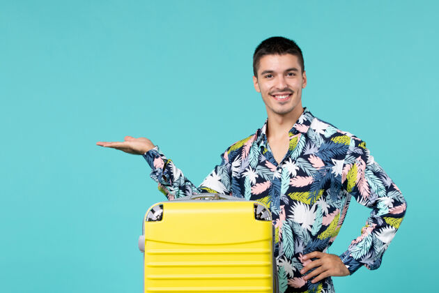 旅行年轻的男性正准备着他的黄色袋子 在淡蓝色的墙上微笑着旅行包微笑快乐