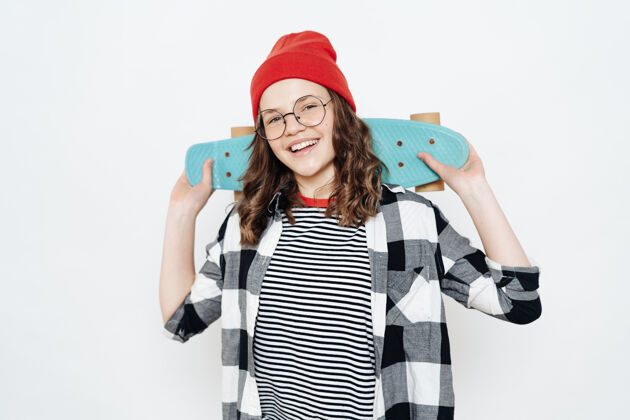 积极快乐时尚的少女少年戴着眼镜 红色的小豆豆 白色的短裤和格子衬衫摆着白色的便士板蓝色板娱乐