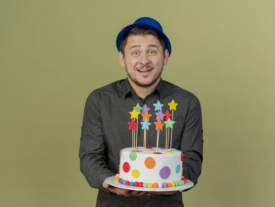 帽子微笑的年轻人穿着黑色衬衫 戴着蓝色帽子 拿着橄榄绿的蛋糕戴着派对拿着