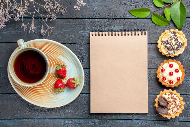 杯子顶视图茶托上的一杯茶和草莓干花枝馅饼叶子和深色木桌上的一本笔记本酸的桌子木头