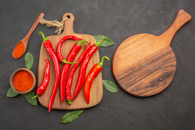 蔬菜顶视图砧板架上放着一碗辣椒粉和红辣椒 黑桌子上放着一把木勺和一个椭圆形的砧板木头新鲜的桌子