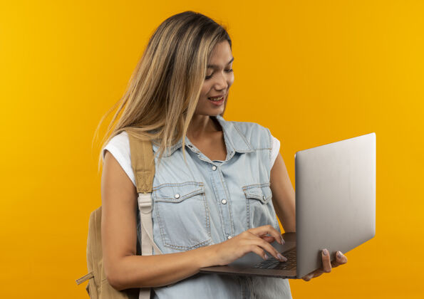 脸很高兴年轻漂亮的女学生戴着背包用笔记本电脑隔离在橙色的墙上女孩橙色年轻