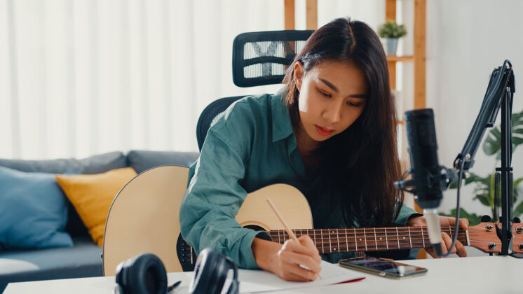 制作快乐的亚洲女词曲作者弹原声吉他 听来自智能手机的歌曲歌曲创作音乐家专业