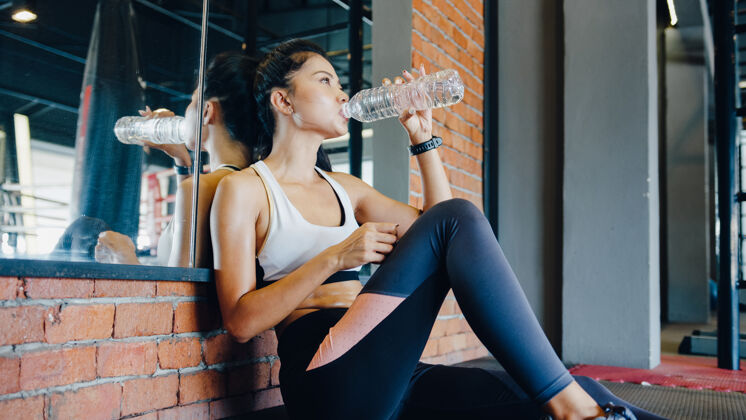 饮食美丽的亚洲年轻女士在健身课上经过脂肪燃烧训练后饮用水锻炼运动装训练西班牙人
