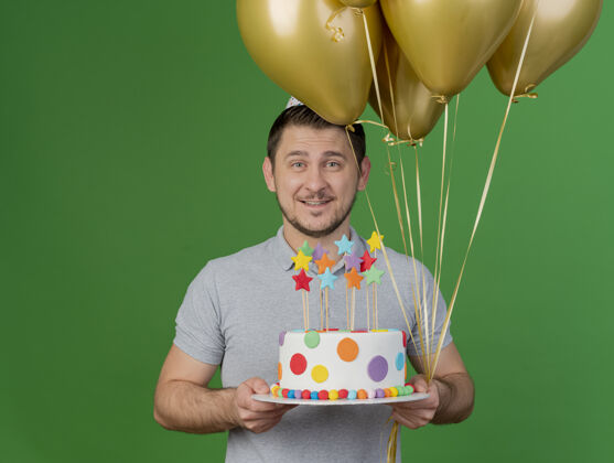 派对戴着生日帽 拿着蛋糕 绿色的气球 面带微笑的年轻人蛋糕戴着帽子