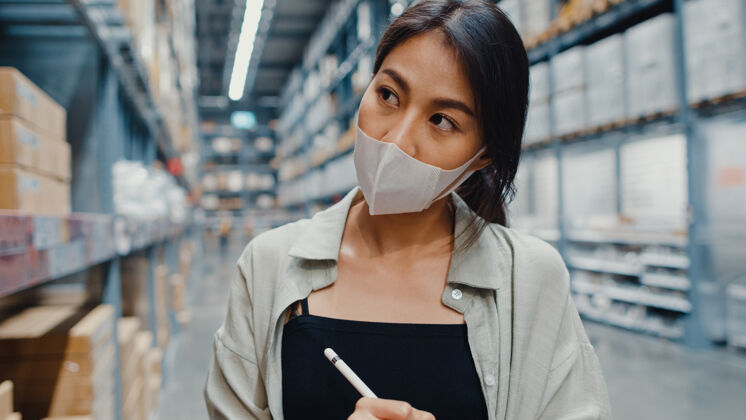 面子年轻的亚洲女商人经理戴着口罩仓库使用数码平板电脑检查库存邮件配送业主
