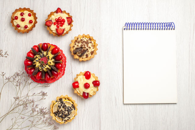 巧克力俯视图浆果蛋糕包围浆果和巧克力馅饼在左侧和一个笔记本在白色木质地面的右侧左浆果右