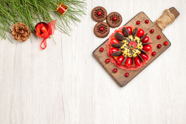 剁碎俯瞰砧板上的浆果蛋糕饼干和松树叶子 白色木质地面上放着圣诞玩具水果冬天叶子