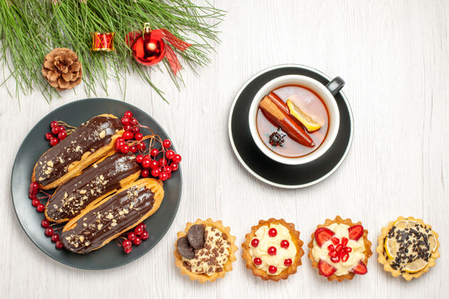 地在灰色的盘子上俯瞰巧克力和醋栗一杯柠檬肉桂茶馅饼和松树叶子 在白色的木质地面上放着圣诞玩具饭松树圣诞