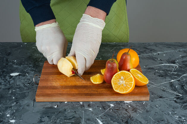 手套男手用刀在桌上的木板顶上切苹果水果男木瓜