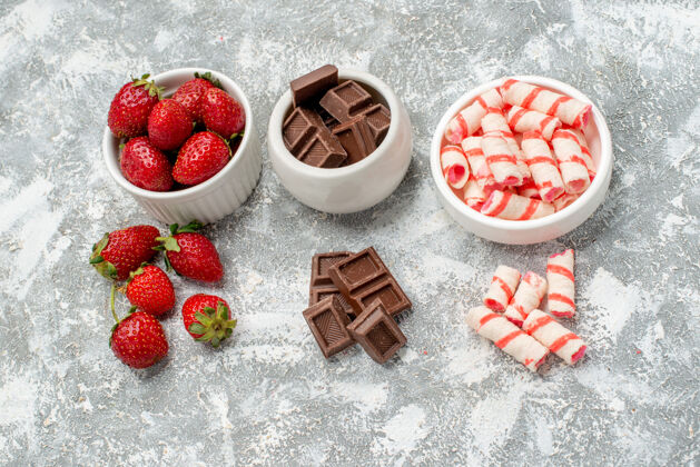 浆果顶视图水平排碗与草莓巧克力糖果和一些草莓巧克力糖果灰白色马赛克地面健康巧克力水果