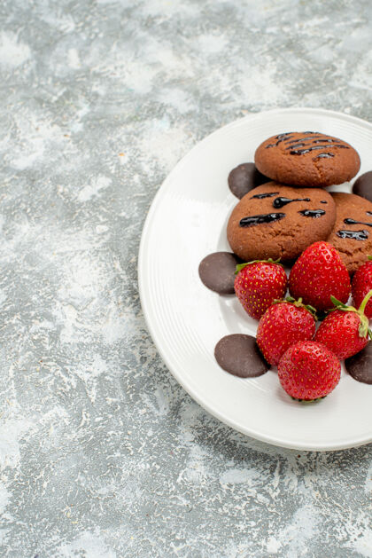 浆果上半部分查看巧克力饼干草莓和圆形巧克力的白色椭圆形盘子在右侧的灰白色地面地面可食用水果椭圆形