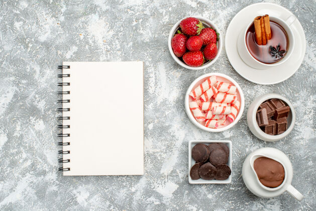空白顶视图碗与可可糖果草莓巧克力茶与肉桂和一个笔记本上的灰白色的表与自由空间笔记本食物相框
