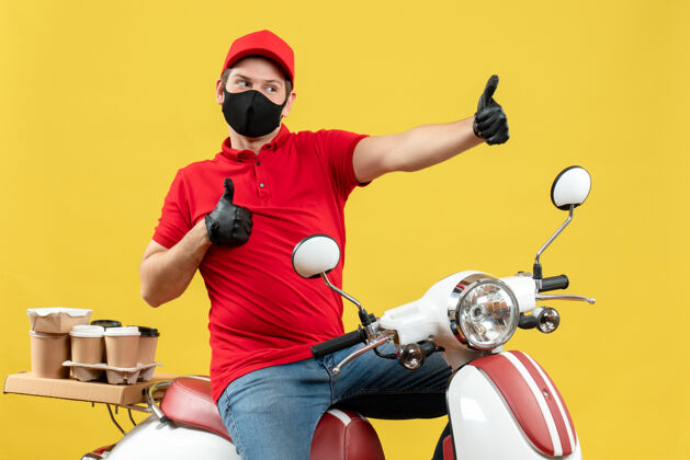 摩托车俯视图自豪自信的年轻人穿着红色上衣 戴着帽子手套 戴着医用面罩 坐在黄色背景的踏板车上传递命令手套帽子男子
