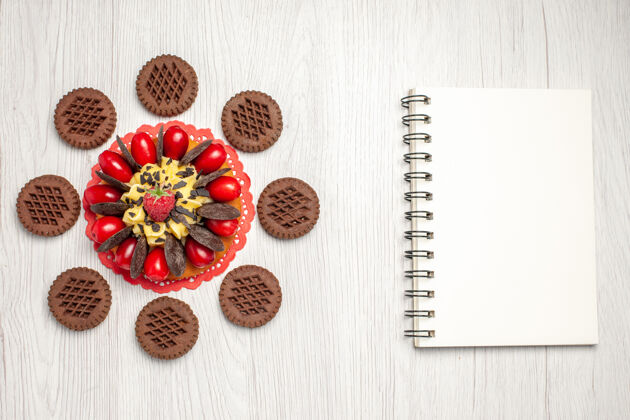 蕾丝俯瞰图红色椭圆形蕾丝装饰布上的浆果蛋糕 白色木桌上放着饼干和笔记本巧克力浆果蛋糕桌子