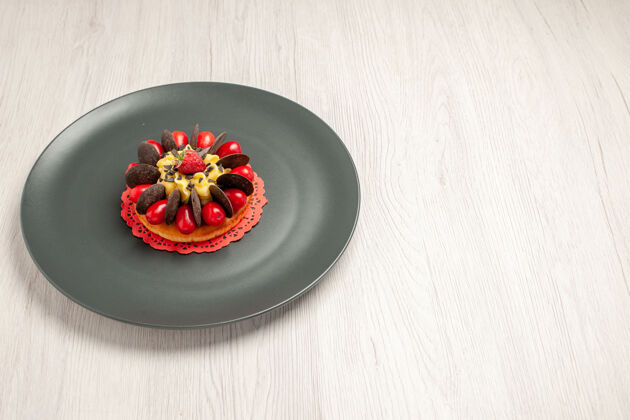圆形左上角是白色木桌上灰色盘子里的巧克力蛋糕 中间有山茱萸和覆盆子设备木材巧克力蛋糕
