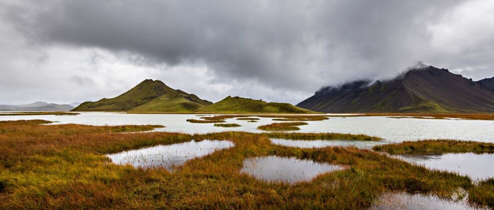 旅游美丽的拍摄在冰岛高原地区的山脉与多云的灰色天空的背景水草地旅游